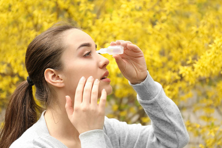 年轻女子用眼药水靠近盛开的树。过敏概念