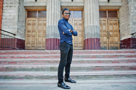 非洲男子在城市街头穿蓝色衬衫和黑色裤子, 帽子和太阳镜