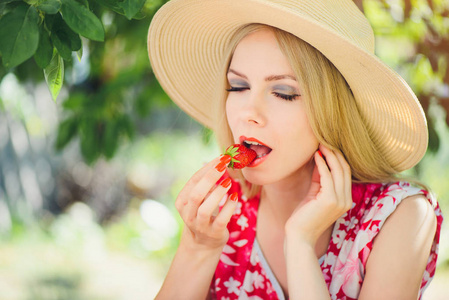 年轻的金发女郎在花园里吃草莓, 夏日阳光明媚, 夏日暖色调, 自我呵护和健康的生活方式