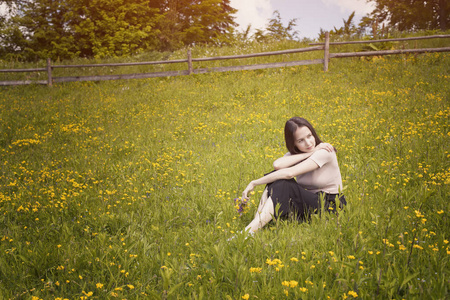 体贴的年轻女子坐在花草甸上。夏日阳光明媚的一天