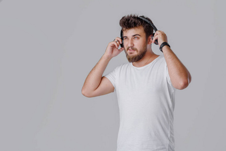 一个戴胡子的年轻人在无线耳机里听响亮的音乐。他不喜欢这些声音