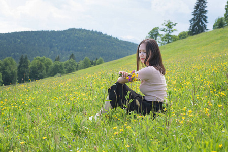 美丽的年轻女子, 鲜花花束坐在草坪上。山上的背景。夏日阳光明媚的一天