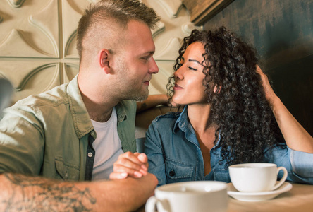 快乐的年轻夫妇是喝着咖啡，微笑着坐在咖啡厅