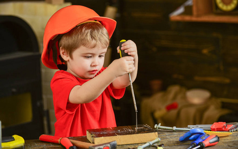 学习使用螺丝刀的孩子。集中的孩子在橙色头盔工作在车间。未来职业概念