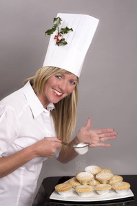 她的帽子将糖粉应用于传统的肉馅饼的冬青树的嫩枝厨师