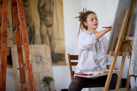 艺术女孩坐在演播室和绘画在画架上