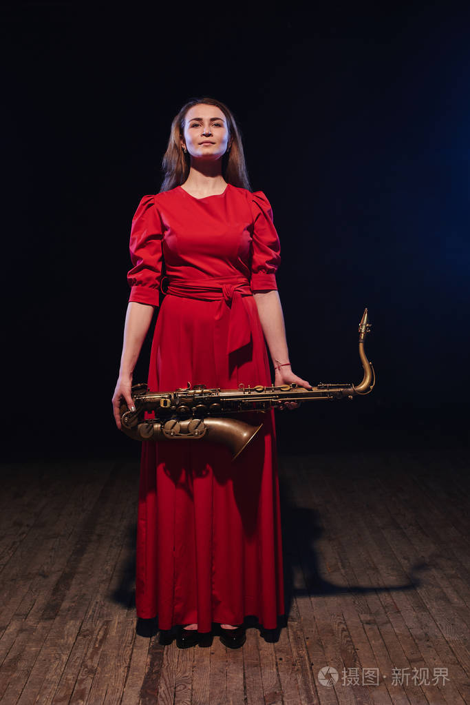 音乐家妇女在明亮的红色礼服拿着萨克斯在手特写