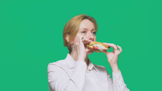 女商人在绿色背景下吃三明治。快速午餐概念