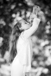 口渴的女孩在自然背景下饮用瓶子里的水。小孩子喝淡水。口渴和脱水。茶点和新鲜。童年与医疗保健, 黑白相间