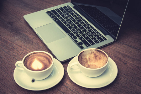 空杯子和充分的咖啡杯子放在一起与笔记本电脑在书桌上