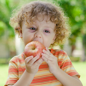 小男孩站在草地上，抱着苹果