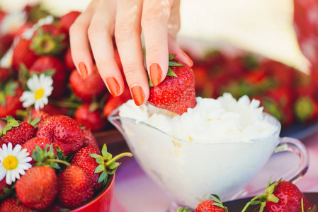 一个新鲜的草莓奶油在一个碗里的一个夏天花园的桌子上装饰着菊花花的手拿着低关键阶段。健康饮食和新鲜度