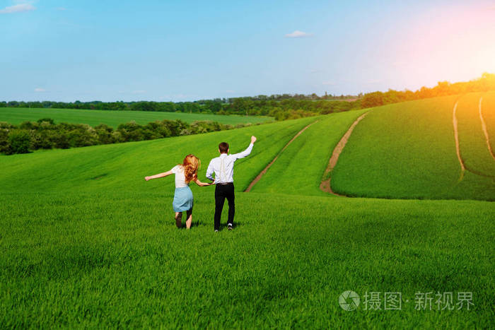 年轻快乐的恋人运行在草地上绿草和蓝天从后面