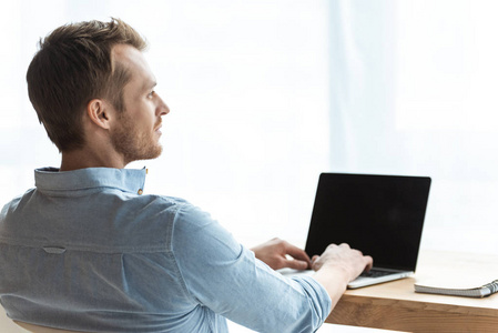 年轻商人在办公室桌子上用空白屏幕在笔记本电脑上工作的后视镜