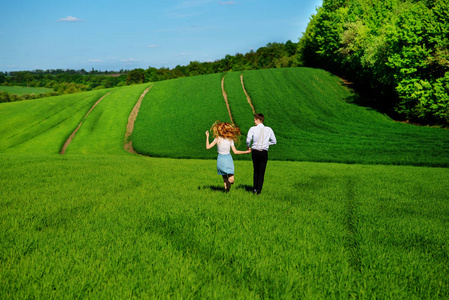 年轻快乐的恋人运行在草地上, 绿草和蓝天, 从后面