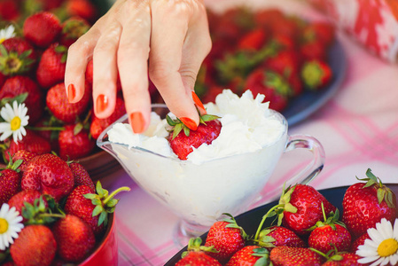 一个新鲜的草莓奶油在一个碗里的一个夏天花园的桌子上装饰着菊花花的手拿着低关键阶段。健康饮食和新鲜度