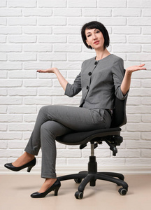 坐在椅子上的女商人穿着灰色西装, 摆在白色的墙前。