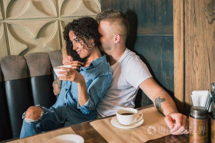 快乐的年轻夫妇是喝着咖啡，微笑着坐在咖啡厅