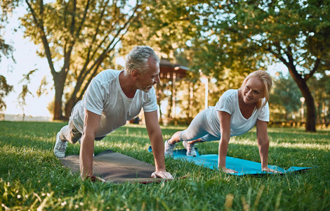 高级夫妇正在户外运动。在日出时在公园伸展。一起做瑜伽。健康的生活方式概念