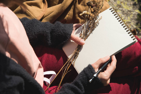 特写在一个女孩手中拿着一个空白的笔记本。在她的手和铅笔一束干的草药。旅游设计师艺术家