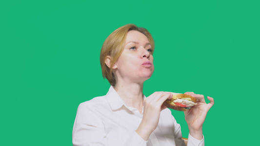 女实业家在绿色背景下吃三明治。快速午餐概念
