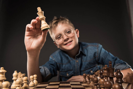 戴眼镜的小男孩选择聚焦灰色背景下国际象棋棋盘上的象棋图