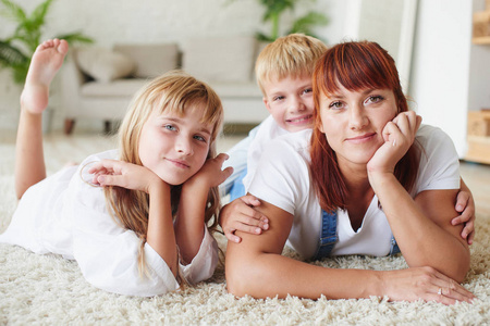 幸福的母亲与女儿和儿子躺在一起地毯在家里