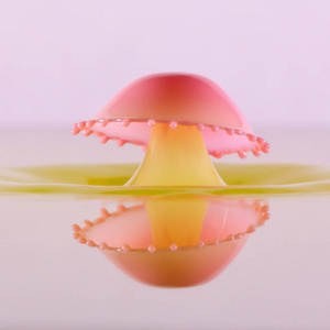 粉红色液体被放入一罐黄色液体中, 两滴碰撞形成伞状, 在液体表面有完美的反射。液滴艺术, 水滴摄影