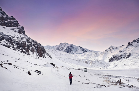 登山者与红色背包走在雪山的紫色天空背景。徒步旅行概念的自由