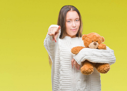 年轻的高加索妇女抱着泰迪熊在孤立的背景指向镜头和你, 手的标志, 积极和自信的手势从前面