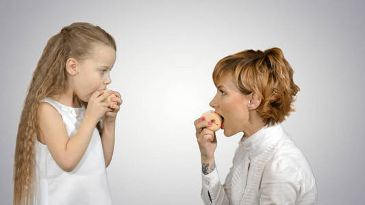 一个年轻的母亲和她的小女儿的肖像在白色背景下吃苹果