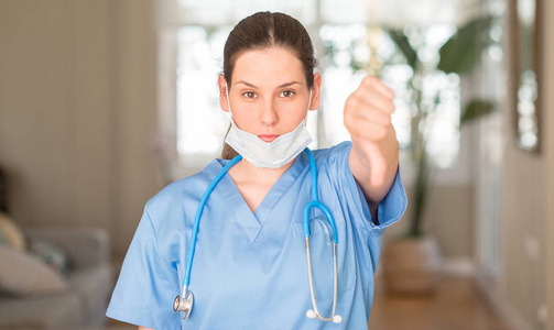 年轻护士妇女戴口罩和听诊器与愤怒的脸, 否定的标志显示不喜欢拇指下来, 拒绝概念