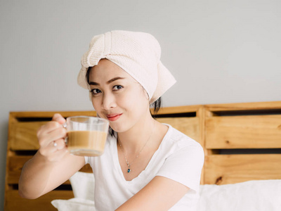 关闭亚洲妇女喝早晨咖啡和放松在她的床后淋浴