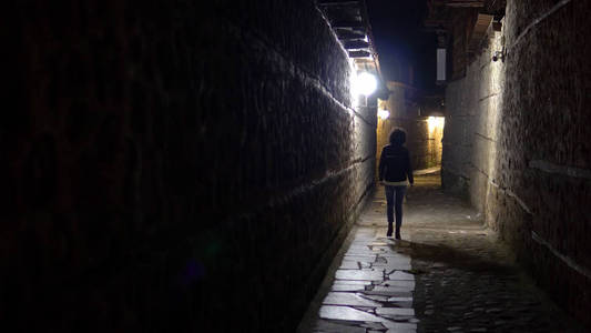 晚上, 孤独的女人走在后街的老石路小巷里照片