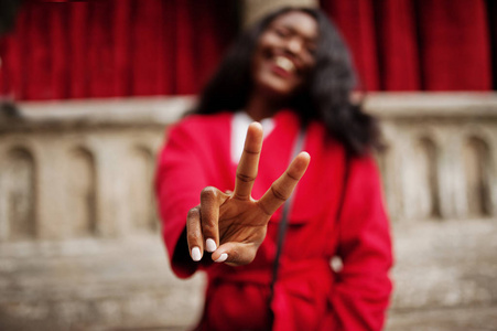 时尚的非洲裔美国妇女在红色大衣对旧列和显示两个手指符号