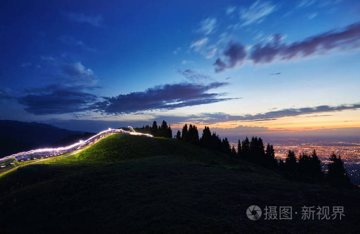 在夜间的山上赛跑的赛跑者的光线痕迹在哈萨克斯坦, 中亚的阿拉木图城市灯