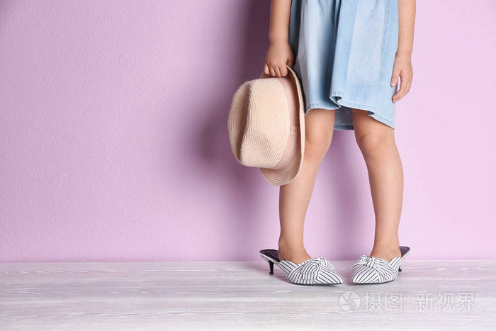 小女孩在超大号的鞋子附近彩色墙壁与空间为文本, 特写在腿照片-正版