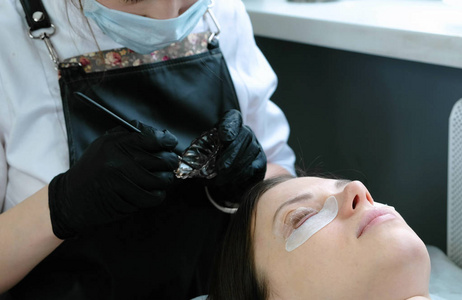 美容治疗。美容师在睫毛上涂上黑色的颜料。肉毒杆菌和复合睫毛