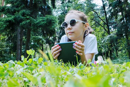 夏日阳光明媚的一天。可爱的女孩在太阳镜躺在绿色的草坪上, 她的小工具。女孩在草地上休息
