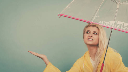 金发女人穿着黄色的雨衣透明打伞检查如果下雨的天气