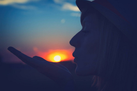 妇女在帽子送空气亲吻在日落在天空背景