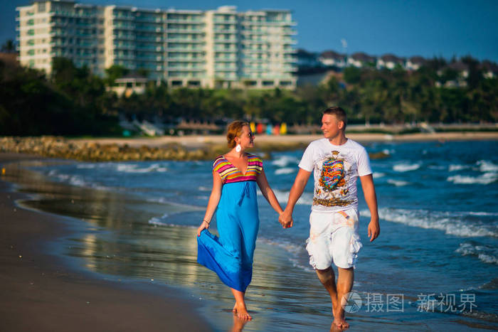 快乐的年轻夫妇沿着海洋漫步在度假村