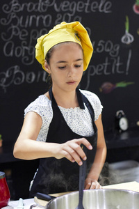 小女孩在厨师的帽子厨师在一个大平底锅在黑厨房里