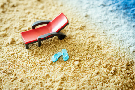 红色玩具甲板椅子和小蓝色触发器在沙子旁边在海在夏天