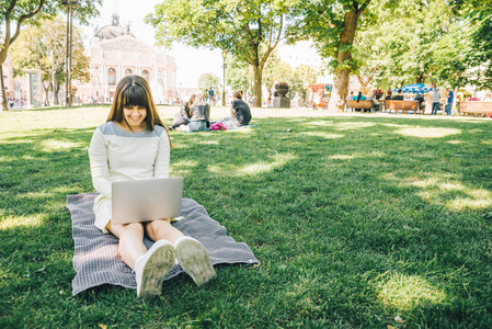 绿色草地上的城市公园里躺着笔记本电脑的年轻成年女子