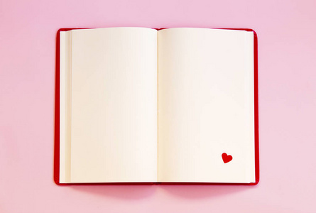 打开笔记本与红色的心脏在粉红色的背景