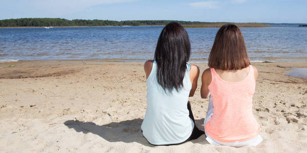后面的两个女人放松的节日女同性恋女孩夫妇在衣服附近的海。两个可爱的女人对蓝天假期