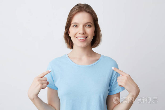 幸福自信的年轻女子在蓝色t恤衫微笑着指着自己的手指在两只手被隔绝