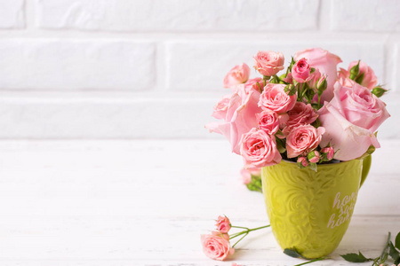 粉红色的玫瑰花在绿色的杯子对白色砖墙。花静物。选择性对焦。文本位置