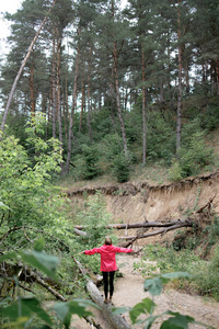 穿着粉红色雨衣的年轻红发女子在森林里漫步, 享受着开阔的空间和自由。自由概念